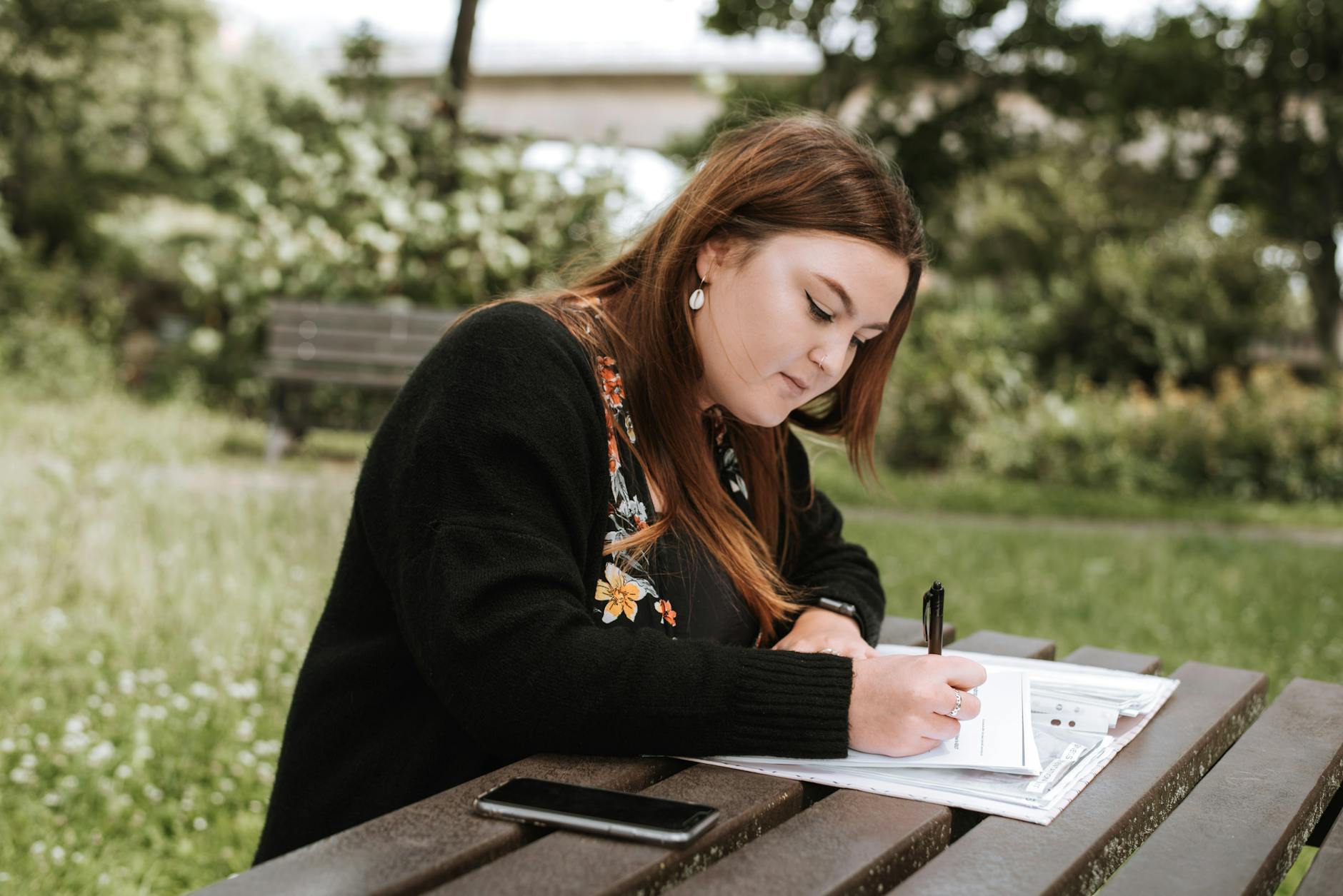 concentrated woman writing notes in papers in park