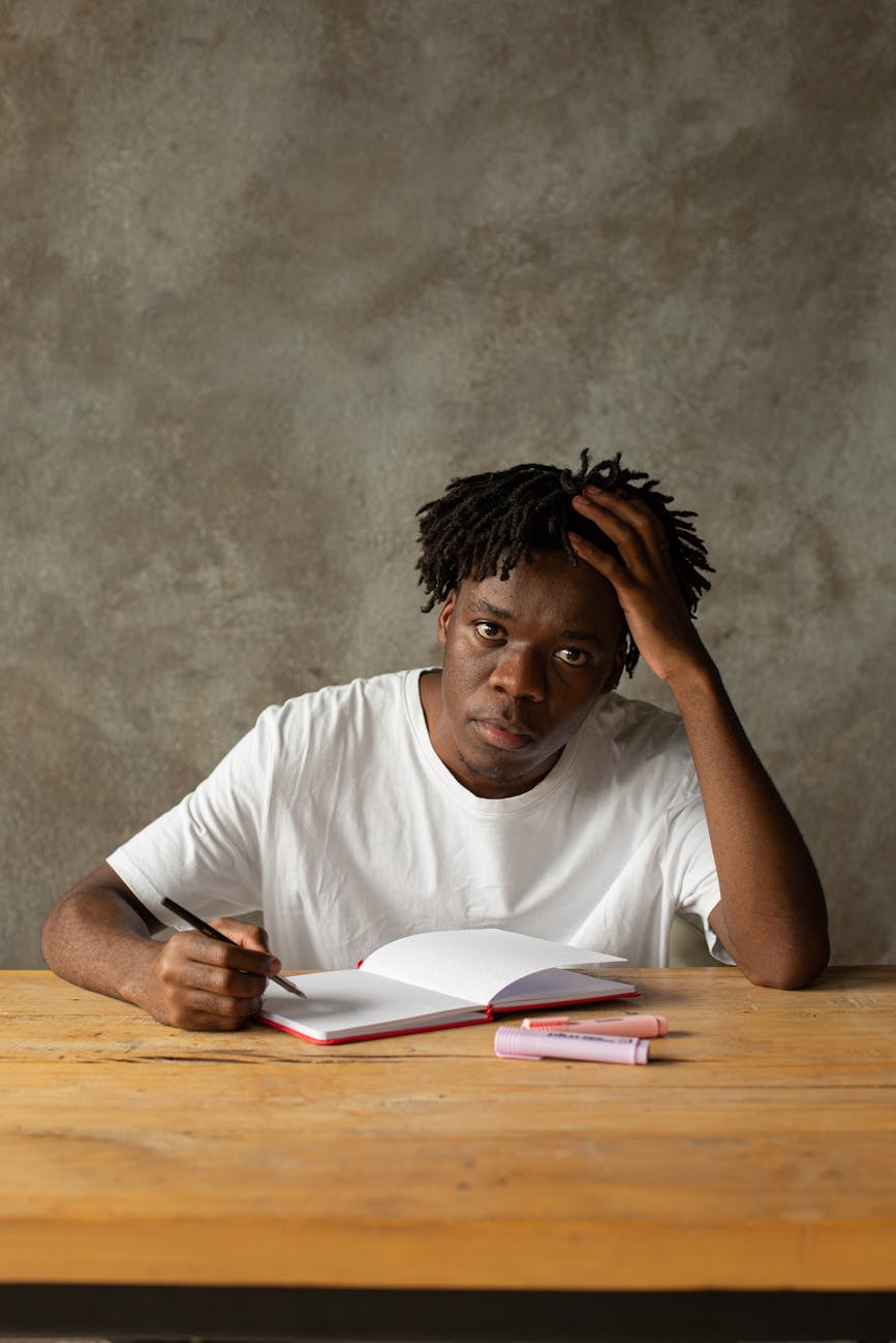 man wearing white t shirt writing on a notebook